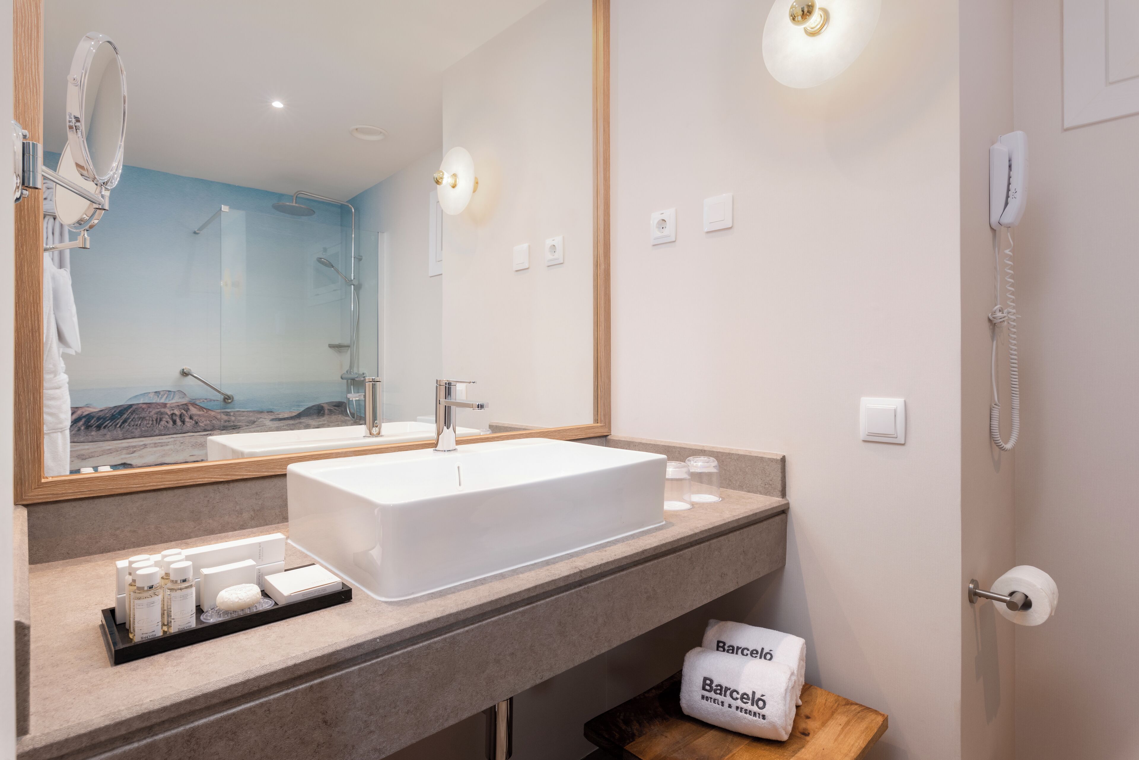 Un baño moderno con un lavamanos grande, un espejo y una ducha. Hay artículos de tocador en la encimera y un perchero para toallas.