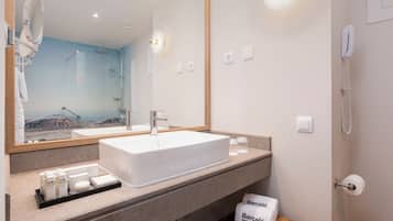 Un baño moderno con un lavamanos grande, un espejo y una ducha. Hay artículos de tocador en la encimera y un perchero para toallas.