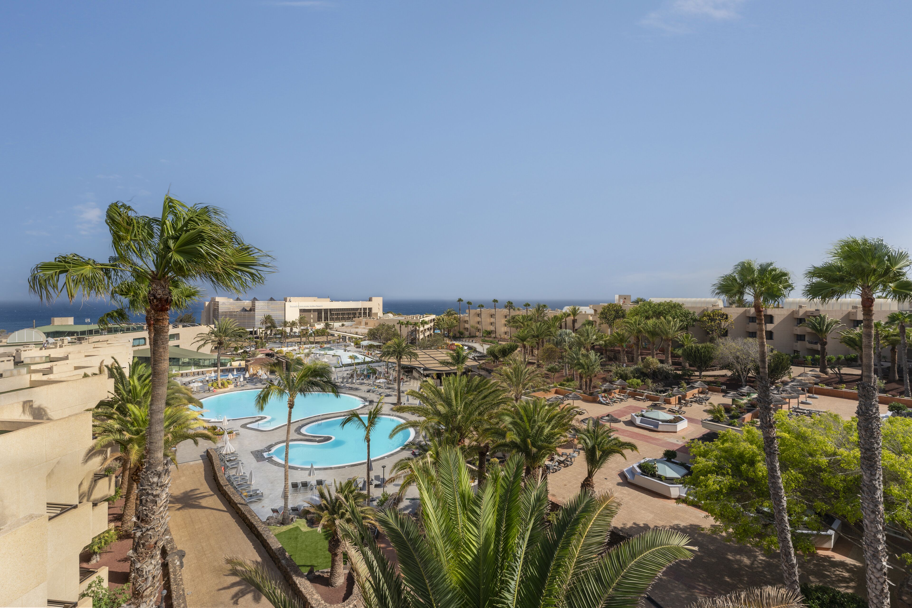 A resort with a large pool, palm trees, and a view of the sea.