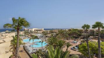 A resort with a large pool, palm trees, and a view of the sea.