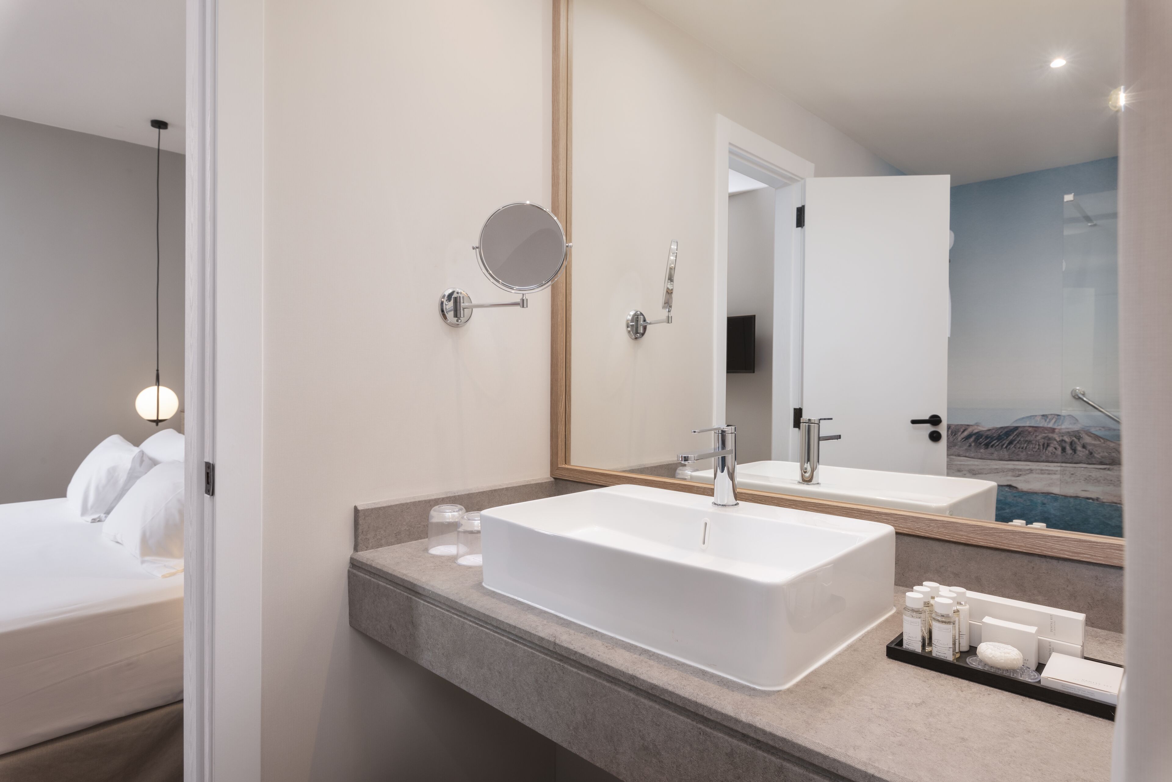Une salle de bain moderne avec un grand miroir, un lavabo rectangulaire et une table de chevet avec des articles de toilette.