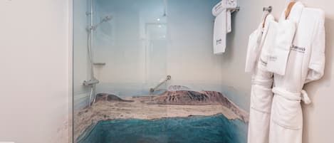 A bathroom with a glass shower enclosure, a white sink, and a towel rack with white robes.
