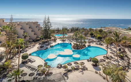 A resort with a large pool, palm trees, and a view of the ocean.