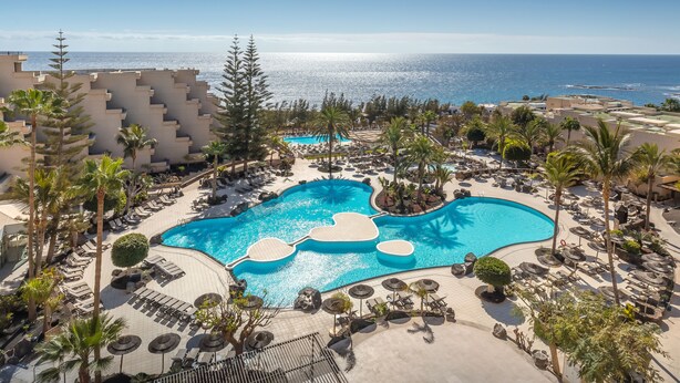 Un resort con una piscina grande, palmeras y vistas al océano.