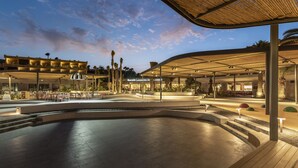 Un espacio al aire libre con una zona de estar curva, una sección cubierta con mesas y un edificio con un letrero que dice "Barcelo Lanzarote Acceo".