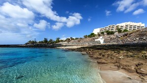 Un hotel frente al mar con costa rocosa, aguas turquesas cristalinas y cielo despejado.
