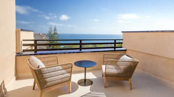 A balcony with two wicker chairs and a small round table, overlooking a clear blue sky and ocean.