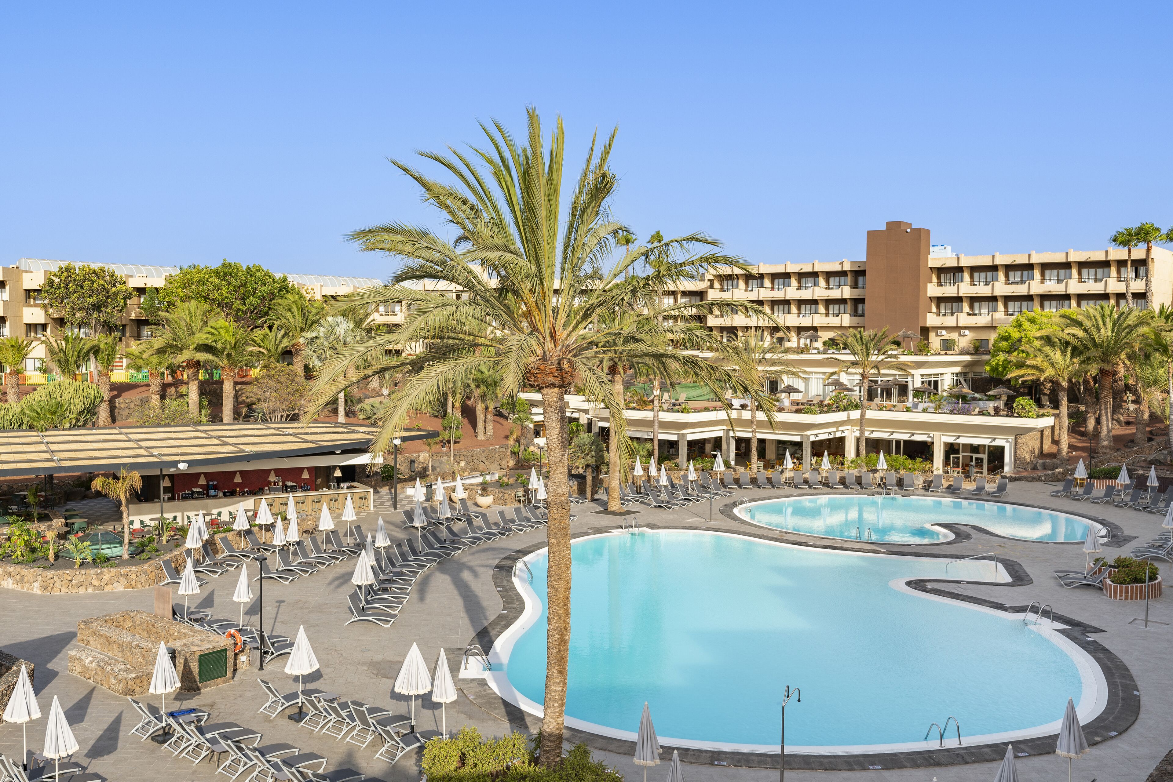 A resort with multiple swimming pools, sun loungers, and palm trees.