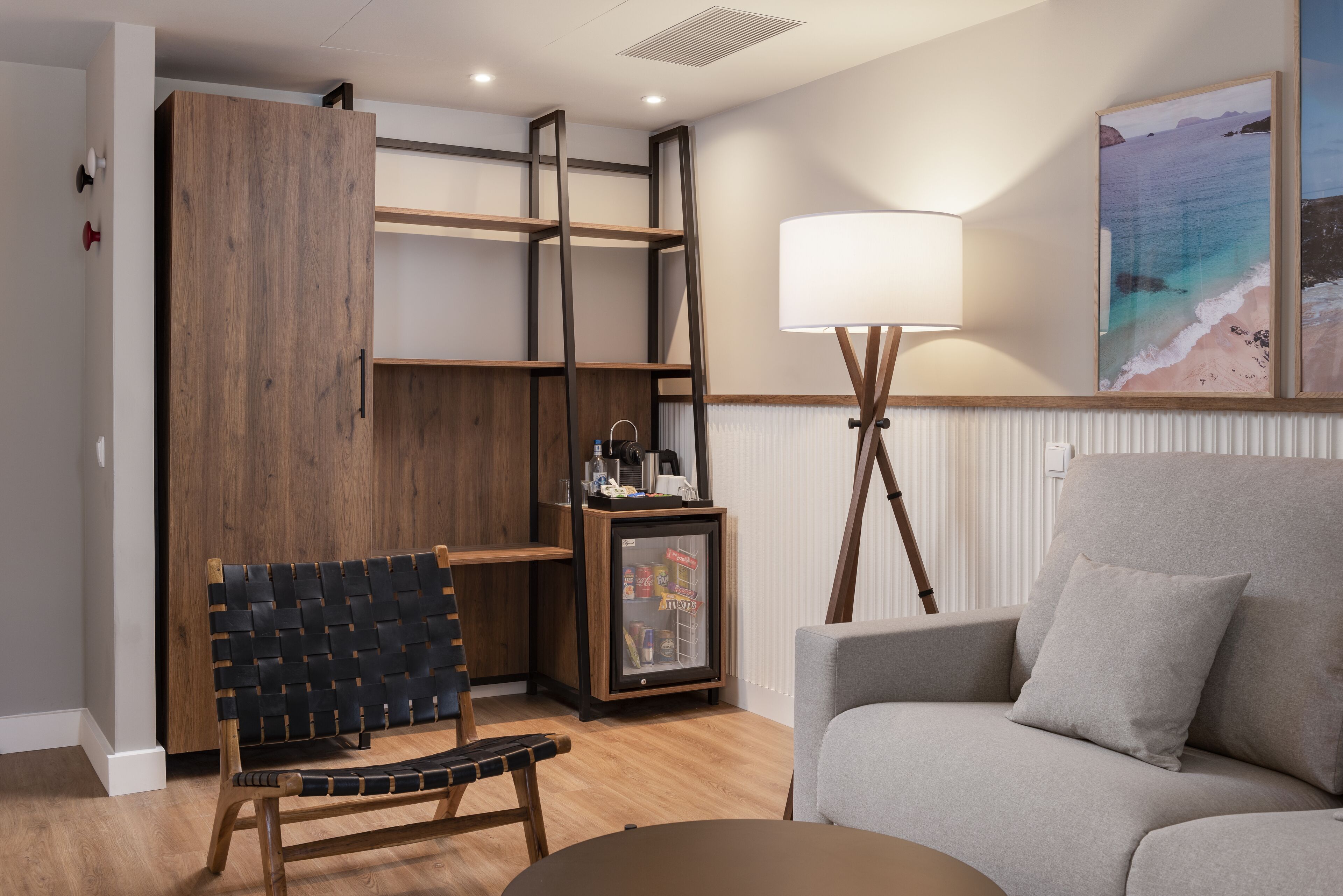 Un salon moderne avec un banc en bois, un canapé gris, une lampe sur pied et un tableau représentant une scène de plage.