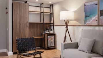 A modern living room with a wooden bench, a grey sofa, a floor lamp, and a framed picture of a beach scene.