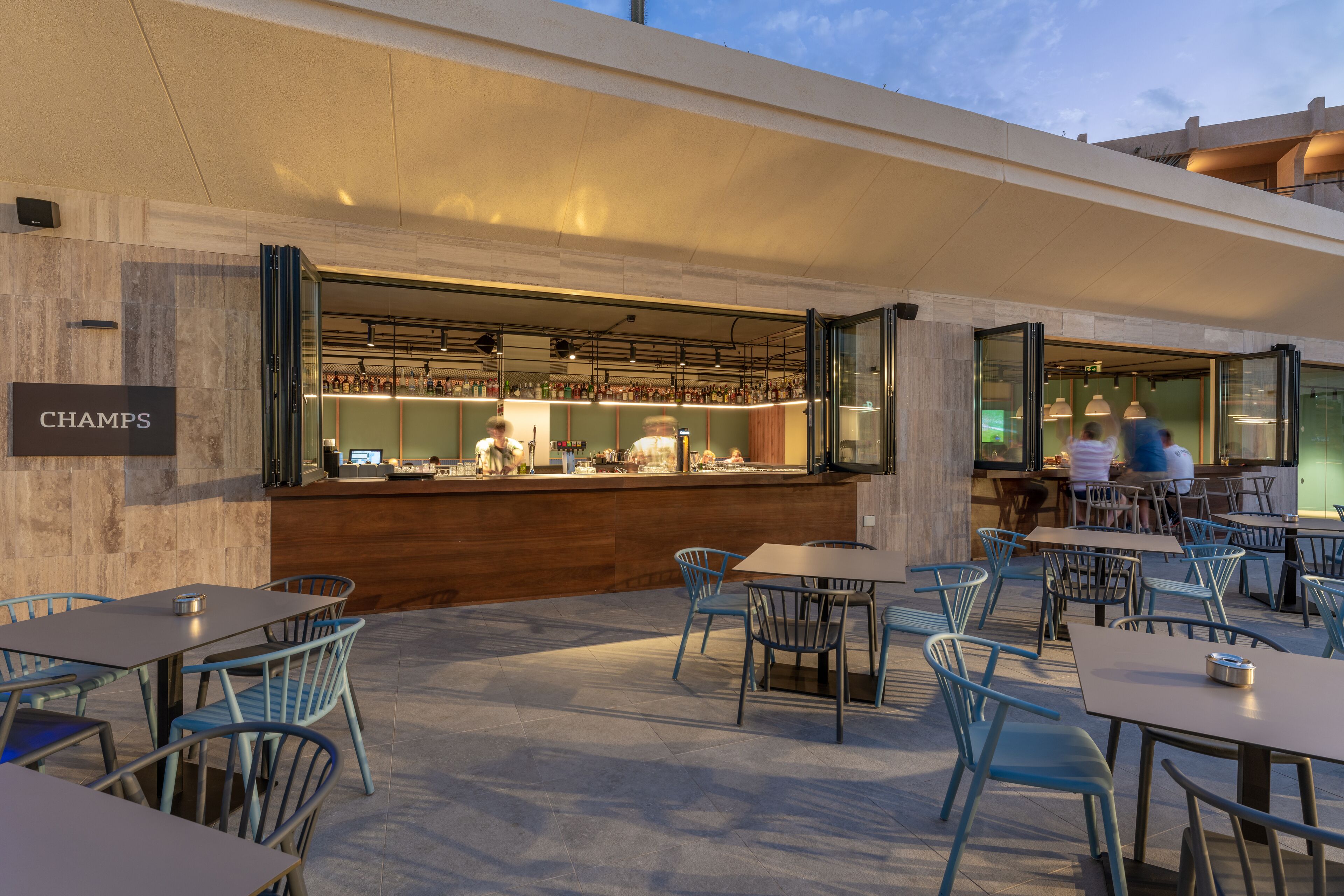 An outdoor seating area with tables and chairs, a bar with a visible counter, and a sign that reads "CHAMPS".