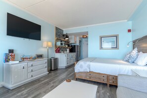 A bedroom with a bed, a dresser, a TV, and a kitchenette. - Beachfront Getaway-06 (Hampton)