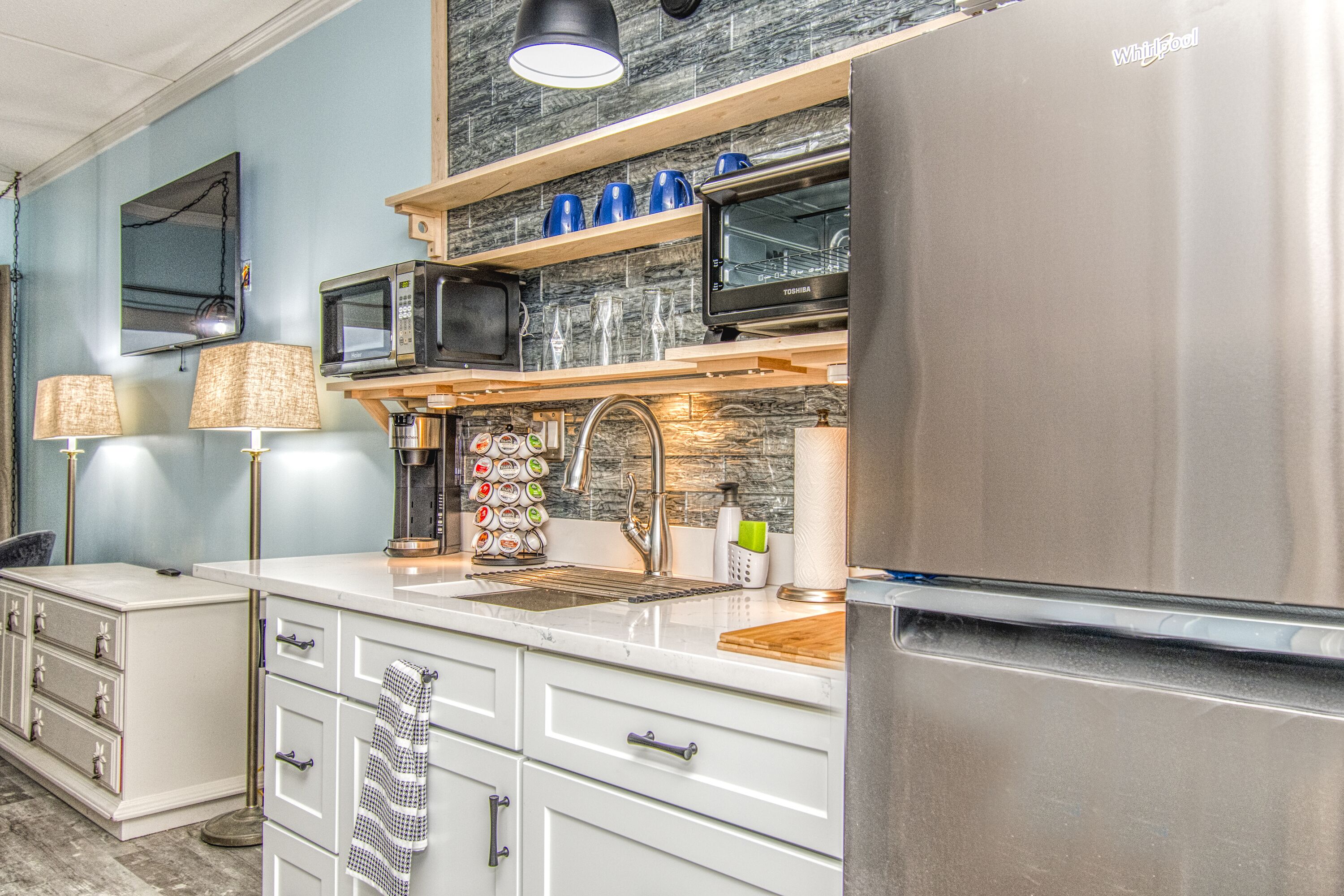 A modern kitchen with a stainless steel refrigerator, a microwave, and a toaster. There are white cabinets and a wooden countertop.