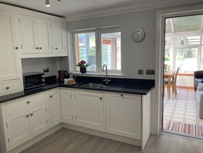 A kitchen with white cabinets, a black countertop, a sink, and a window with a view of the outside. - Beach Cottage Sleeps 4 (2 Bedroom) (Sandhead)