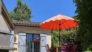 En terrasse med et bord, stole, en rød parasol og en stenvæg.