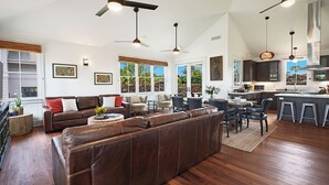A spacious living area with a large brown leather sofa, a dining table with chairs, and a kitchen in the background. - Plantation House by Destination Kauai - Poipu Beach Estates, Central A/C, 3BD (Koloa)