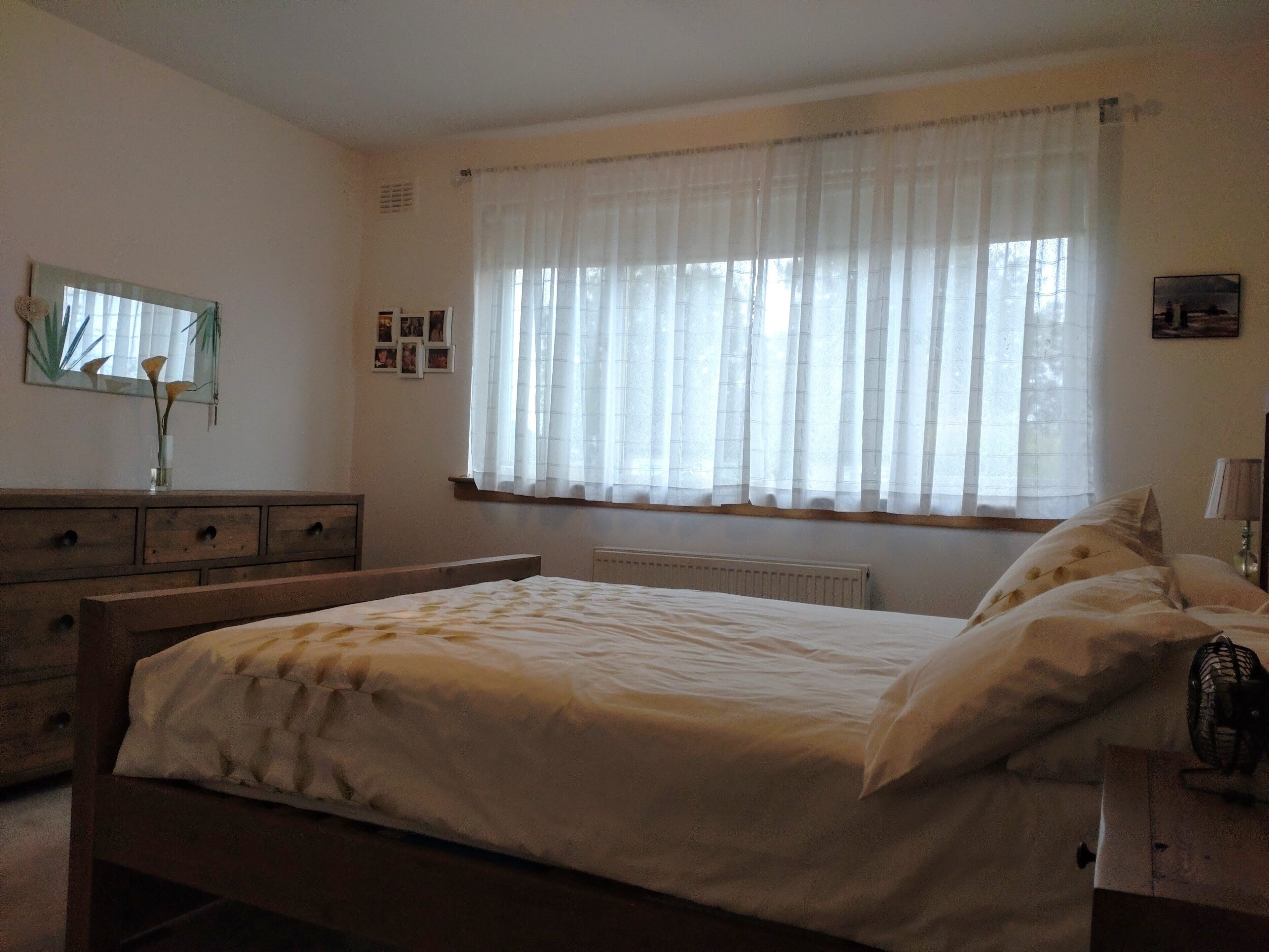 A bedroom with a bed, dresser, mirror, and window with curtains.
