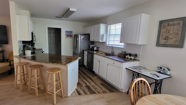 A modern kitchen with white cabinets, a granite countertop, and a built-in island with bar stools. - Private Beach Home (Navarre)
