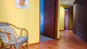 Un pasillo con una silla de mimbre, una puerta y una pared de ladrillo.