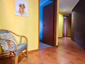 Passadís amb una cadira de vímet, una porta i una paret amb relleu de maó.
