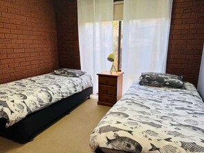 Ein Zimmer mit zwei Betten, einem Holznachttisch und einem Fenster mit transparenten Vorhängen.