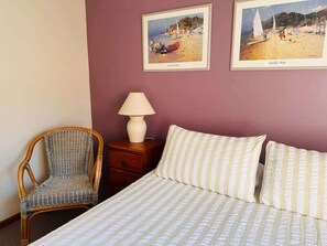 Ein Schlafzimmer mit einem Bett, einem Sessel, einem Nachttisch und zwei gerahmten Bildern an der Wand.