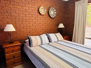 Ein Schlafzimmer mit Backsteinwand, einem Bett mit gestreifter Bettwäsche, zwei Nachttischen mit Lampen und zwei Wanduhren.