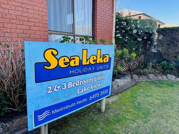 Cartell de Sea Leka Holiday Units que anuncia apartaments de 2 i 3 habitacions amb vista al llac, gestionats per Merrimulla Realty.