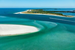 An aerial view of a coastal area with clear turquoise waters, a sandy beach, and a small island with buildings.