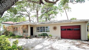 Une maison de plain-pied avec une porte de garage rouge, un porche à l’avant et un soleil décoratif peint sur le mur.