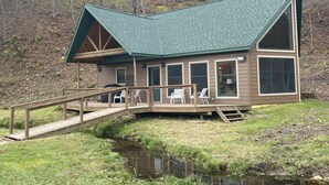 A cabin with a green roof, large windows, and a wooden deck with chairs. - Cabin in Beautiful Timber Coulee (Westby)