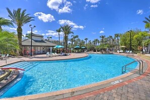 A swimming pool with lounge chairs and umbrellas, surrounded by palm trees and a building with a tiled roof. - Lakeview Condo  minutes to Convention Center, Disney & Universal Studio (Orlando)
