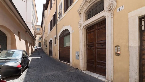 A narrow cobblestone street flanked by historic buildings with arched doorways and a car parked on the left. - Quiet roof terraces close to trevi fountain (Roma)