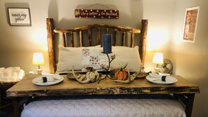 Une chambre à coucher au style rustique, avec une tête de lit en bois, une couvre-lit matelassé et une table de chevet agrémentée d’une lampe et d  ’objets décoratifs.