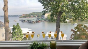 Une table avec des boissons et une plante près d’une fenêtre donnant sur un lac où l’on peut voir des bateaux.