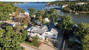 Un quartier résidentiel avec des maisons situées près d’un lac, où l’on remarque une maison imposante avec un toit gris et des murs blancs, entourée d’arbres et d’une jetée.
