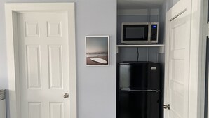 Eine kompakte Küche mit einer weißen Tür, einem schwarzen Kühlschrank, einer Mikrowelle und einem gerahmten Bild an der Wand.