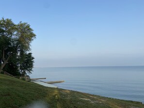 A coastal view with a grassy area, trees, and a calm sea. - 3 Little Cottages - #2 Sunburst Cottage (Geneva)
