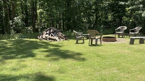 Ein grasbewachsener Außenbereich mit Holzstoß, mehreren Plastikstühlen und einem Feuerkorb.