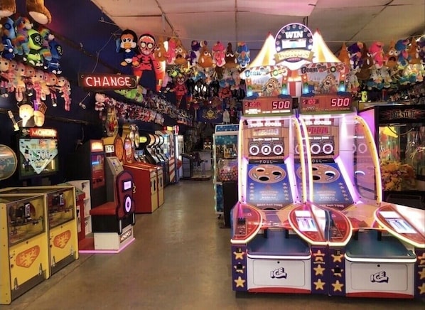 A row of arcade games with plush toys hanging above, including a 'Change' sign and 'Bean Bag Toss' machines.