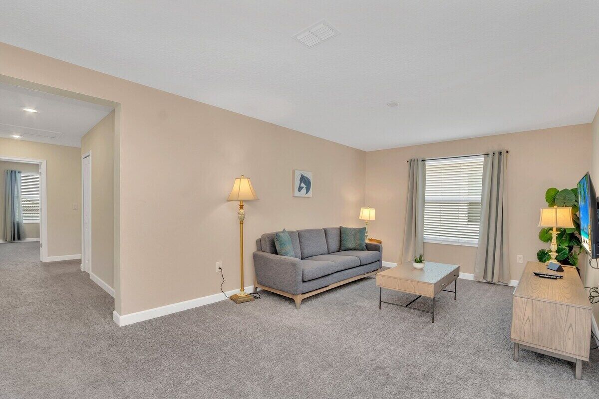A living room with a grey sofa, two side tables with lamps, a small coffee table, and a TV on a wooden cabinet.
