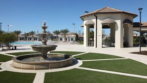 Un patio con una fuente central, un pabellón y una piscina al fondo.