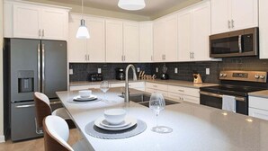 A modern kitchen with white cabinets, stainless steel appliances, and a central island with seating. - Amazing 6Br Villa Near Disney With Lake View(8972) (Reunion)