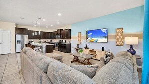A modern living room with a grey sofa, a dining table, and a kitchen in the background.
