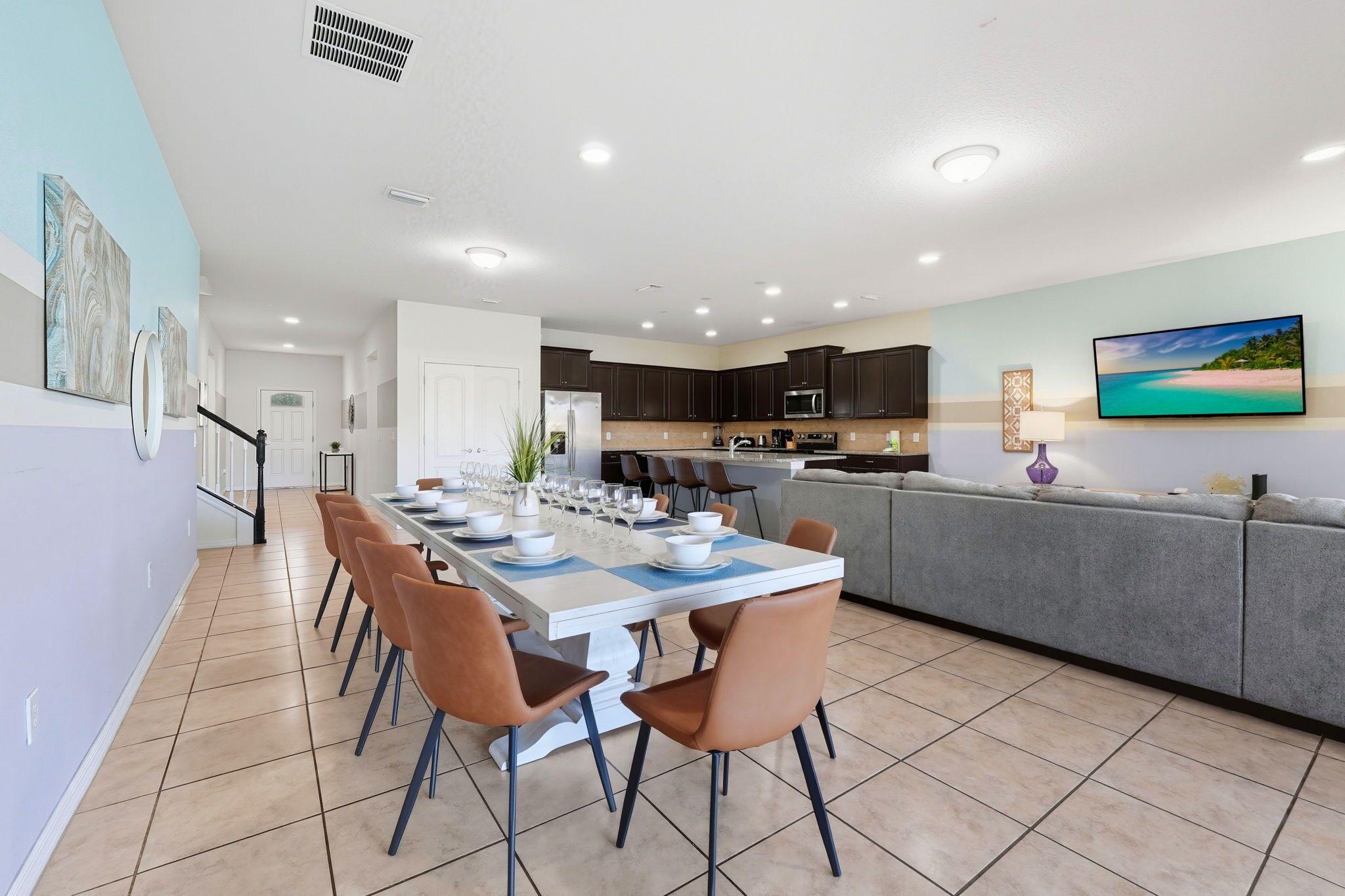 Une cuisine moderne avec des meubles de couleur sombre, un grand îlot central et un coin repas comprenant des chaises et une table dressée pour six personnes.