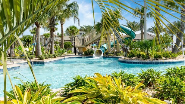 Une piscine avec un toboggan, entourée de palmiers et bordée d’un bâtiment doté d’un balcon.