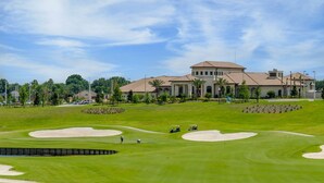 Un parcours de golf avec des bunkers, un club-house et un grand bâtiment en arrière-plan.