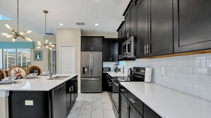 A modern kitchen with dark cabinets, a stainless steel refrigerator, a microwave, and a dishwasher. - Ultimate 5Br Villas With Pool/Spa (1555FD) (Davenport)