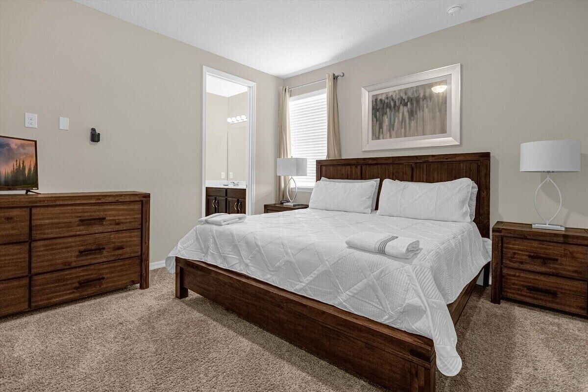 Une chambre à coucher avec un lit en bois, une commode, une table de chevet, une lampe et un tableau au mur.