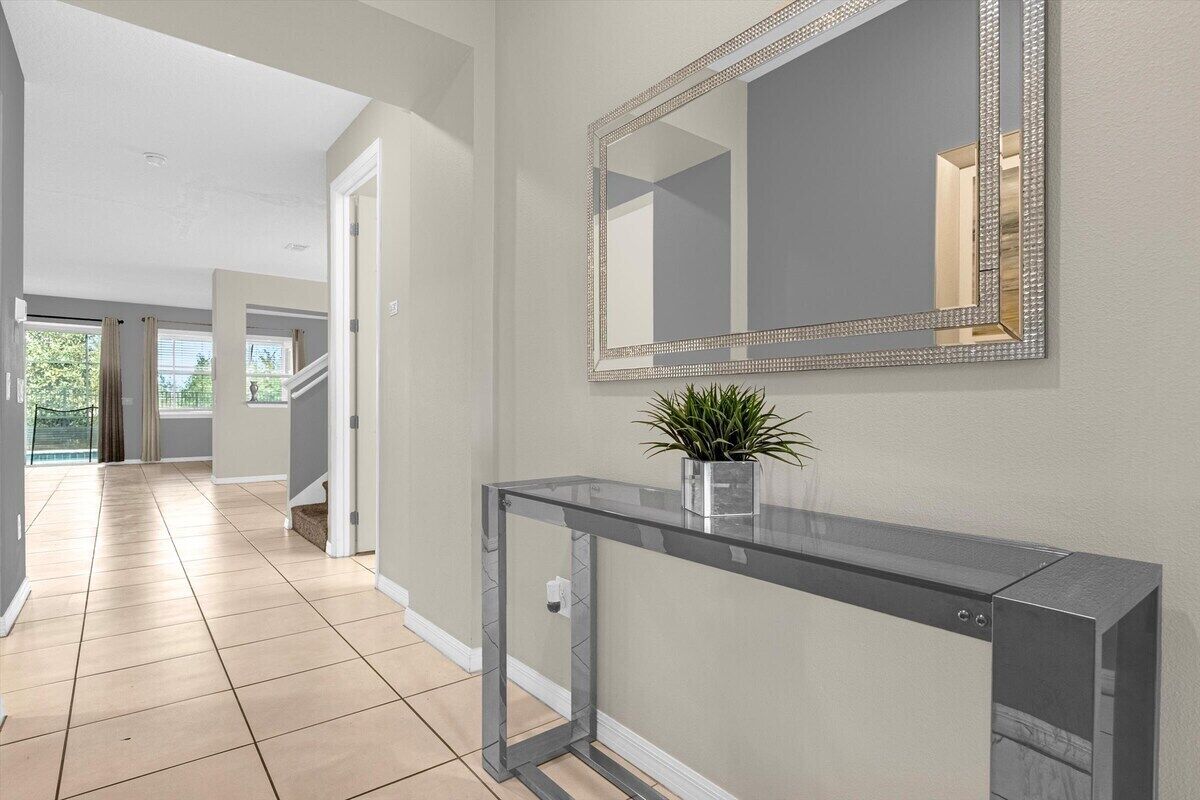 A hallway with a glass console table, a mirror with a decorative frame, and a potted plant.